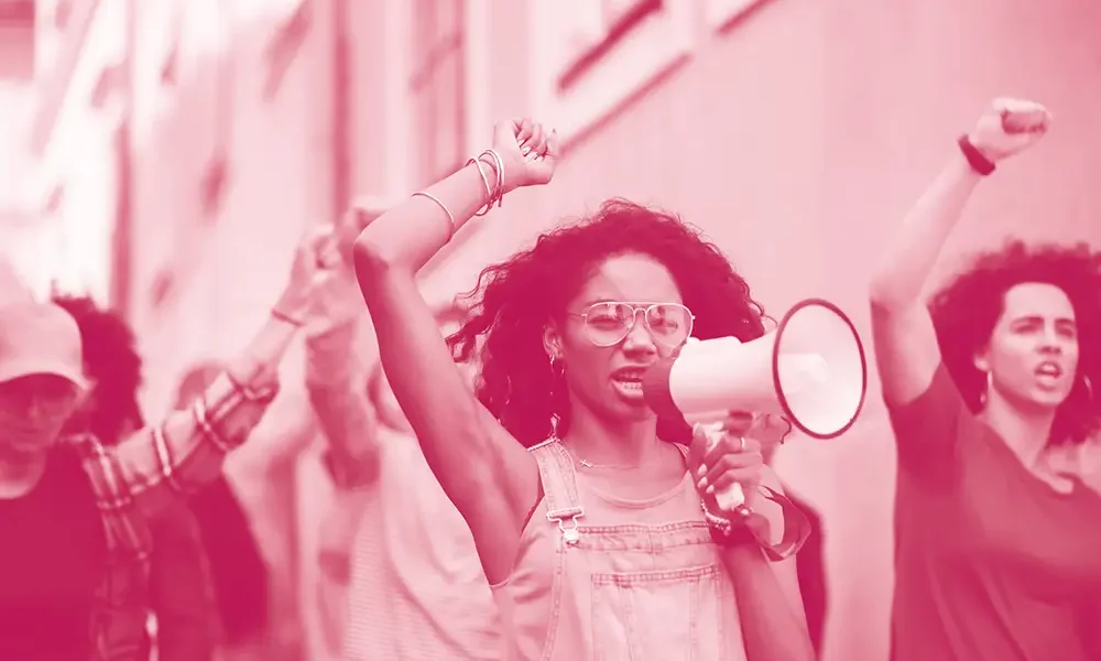 Woman holding a megaphone, fist raised in the air, leading a group of people in a protest